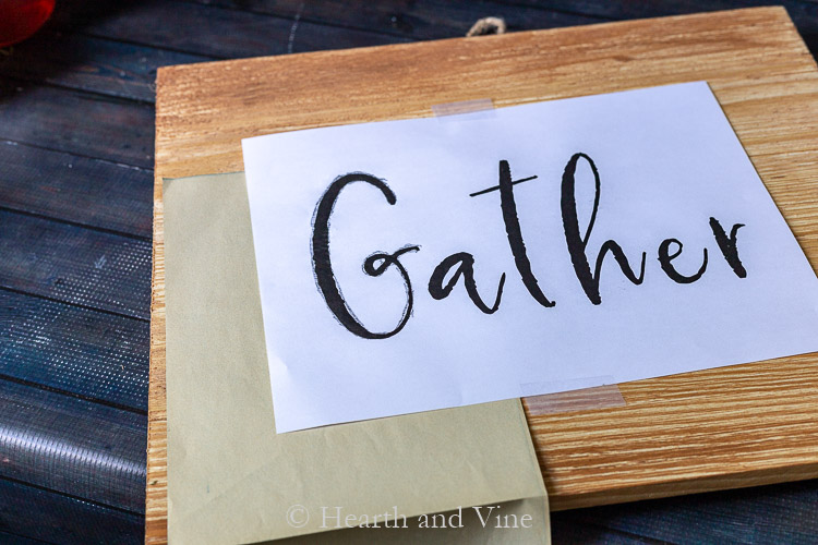 Tracing the word Gather on wood sign