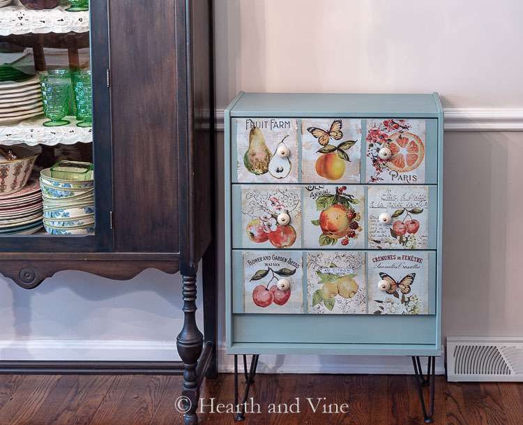 Three drawer chest painted blue and decorated with botanical decals next to a china cabinet