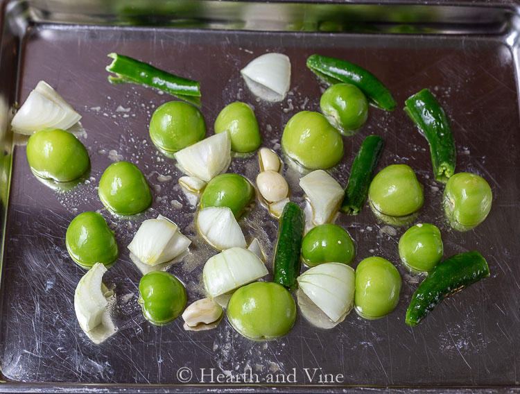 Tomatillos, onion, peppers and garlic on cookie sheet with olive oil