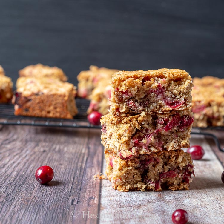 Stack of three cranberry oatmeal bars and scattered fresh cranberries