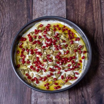 Goat cheese dip in a round pan with pistachios and pomegranate seeds.