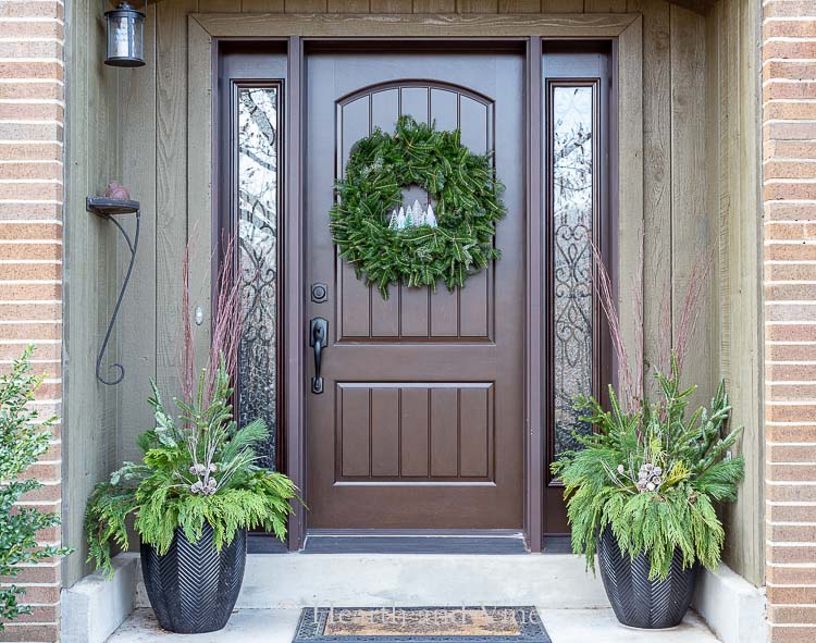 Front porch with bottle brush tree wreath on door and evergreen planters on sides