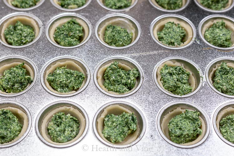 Mni muffin tin with dough cups filled with cheesy spinach filling