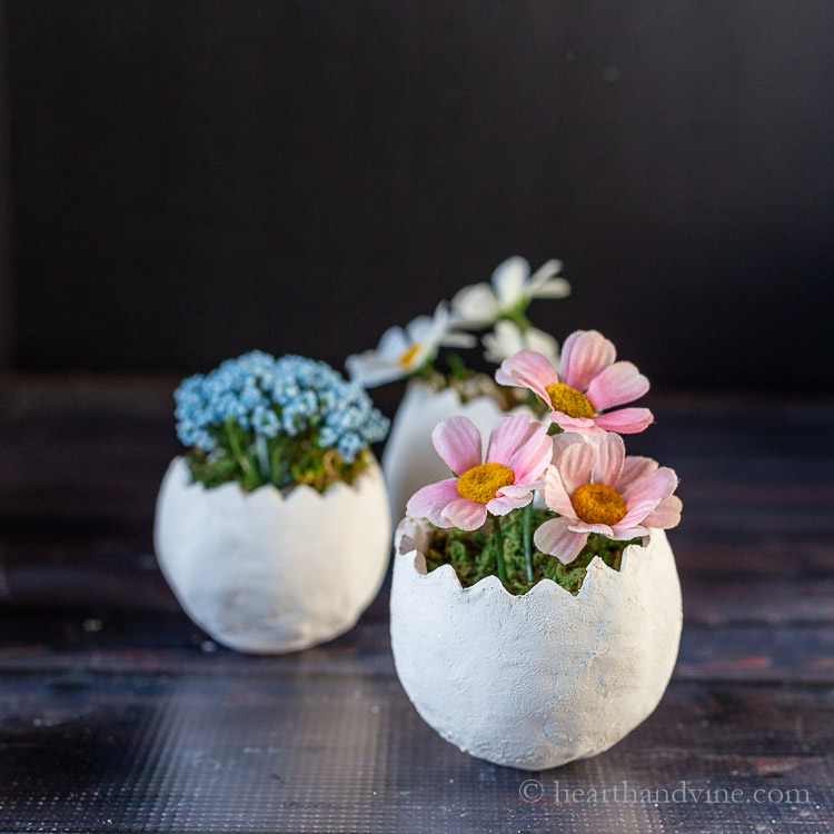 Three small clay egg planters with artificial flowers