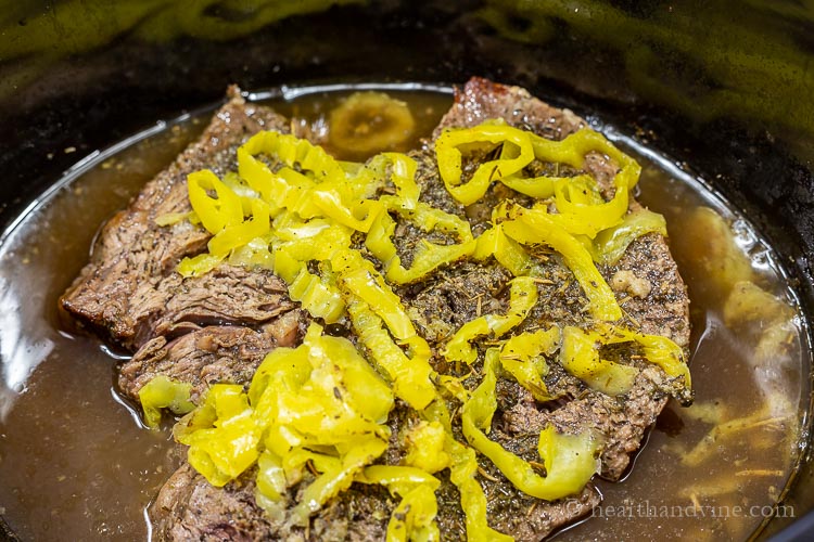 Cooked chuck roast in slow cooker with hot pepper rings and seasonings