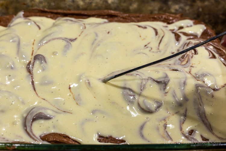 Cheesecake layer on brown batter and toothpick making swirls