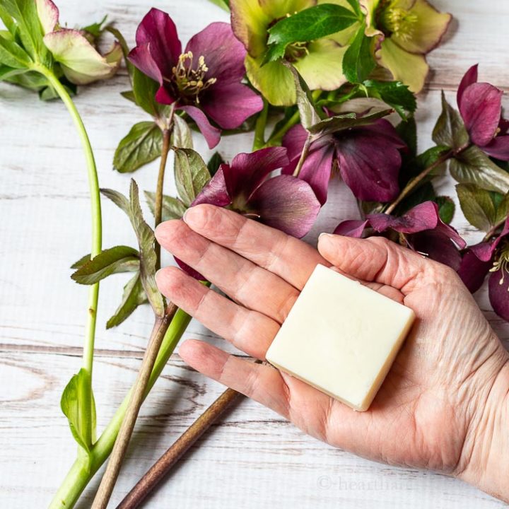 Lotion bar in palm of hand above flowers