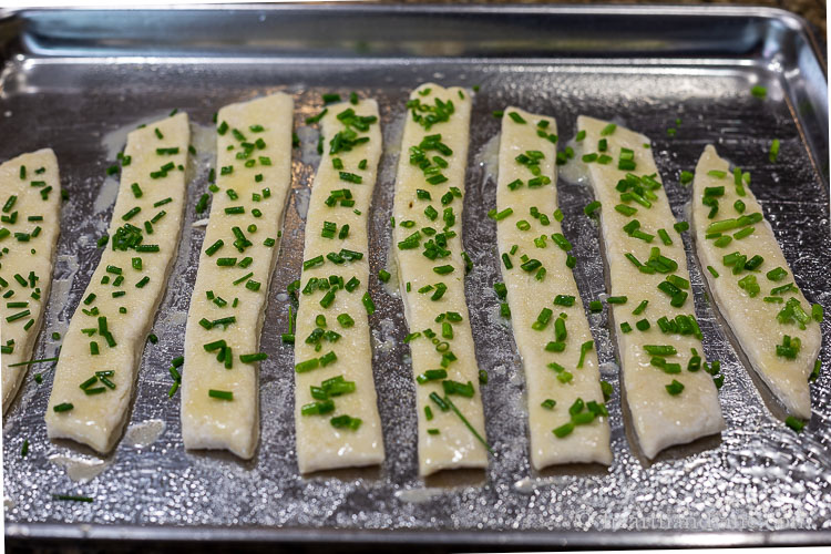 Breadsticks on an oven tray topped with melted butter and chopped fresh chives.
