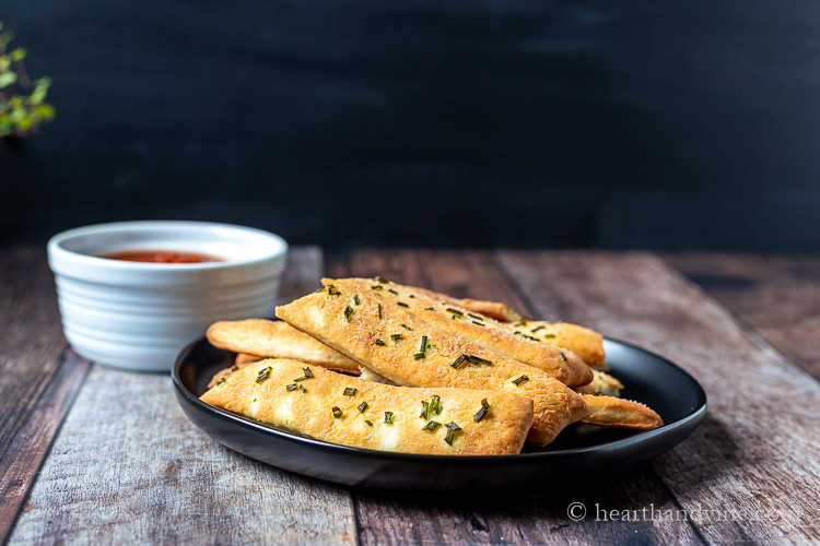 Plate of chive breadsticks and small bowl of marinara sauce.