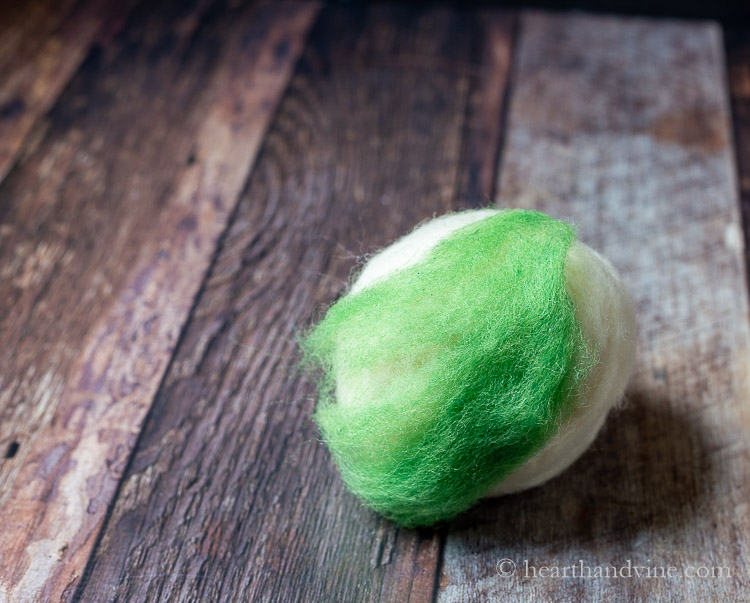 Adding a piece of green wool roving to the natural ball.