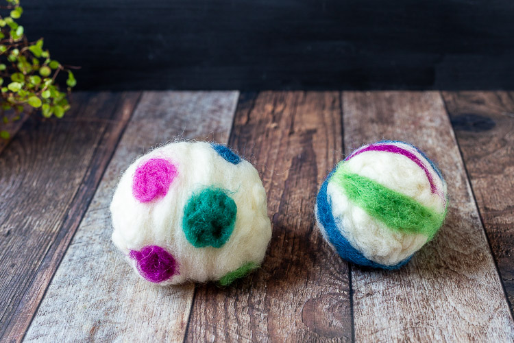 Different colors of wool roving adding in stripes and dots on two dryer balls.