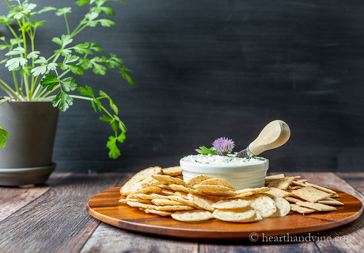 Crackers and a bowl of blue cheese spread on a tray with a knife and chive blossom decoration.