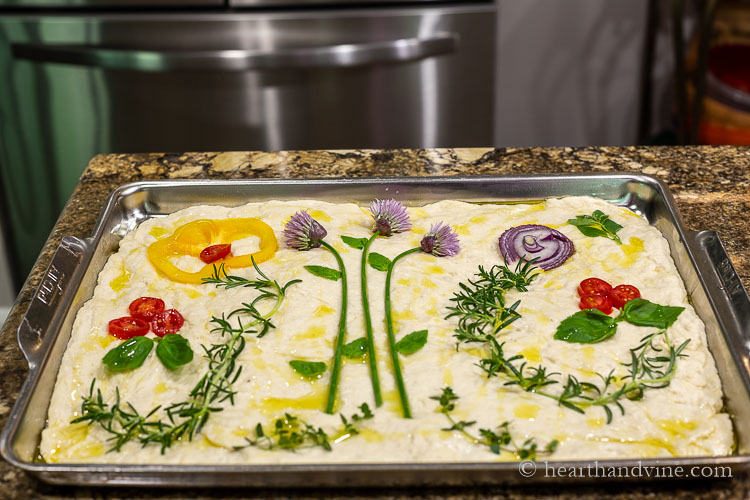 Fresh herbs and vegetables arranged on focaccia dough.