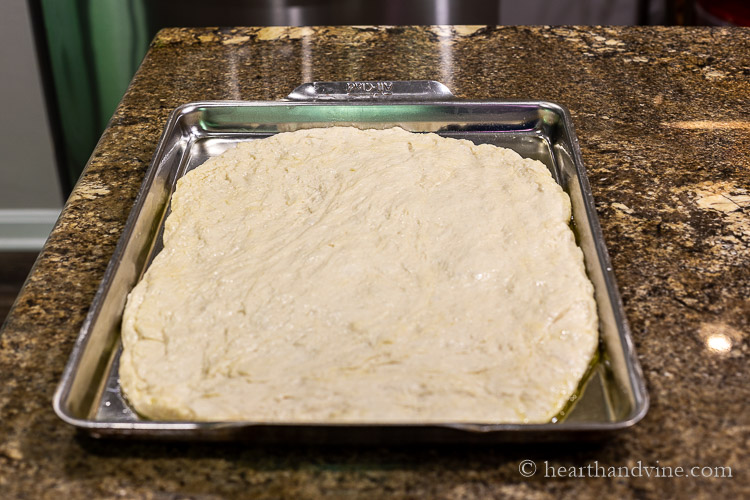 Spreading focaccia dough into baking pan.