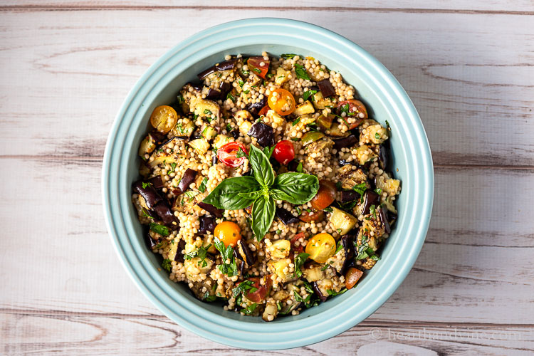 Aerial view of grilled eggplant salad in a large blue bowl garnished with basil leaves in the center.