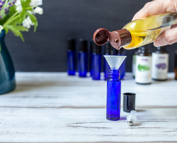 Jojoba oil poured into a funnel in a cobalt roller bottle