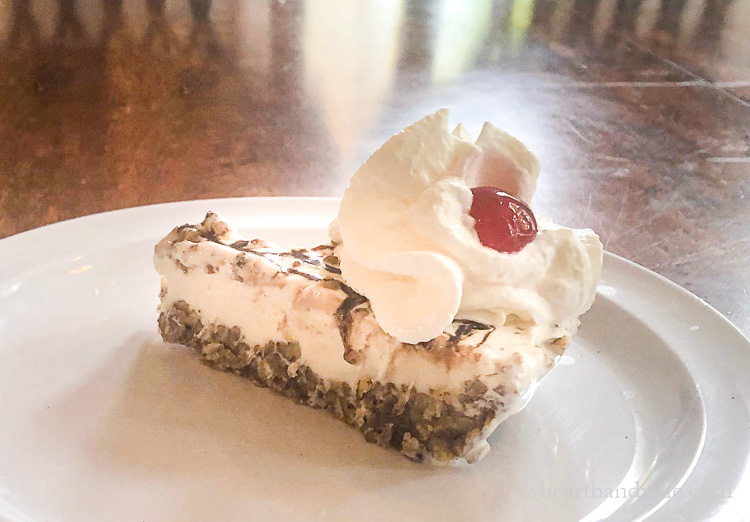 Slice of pecan ball pie with whipped cream and a cherry on top.
