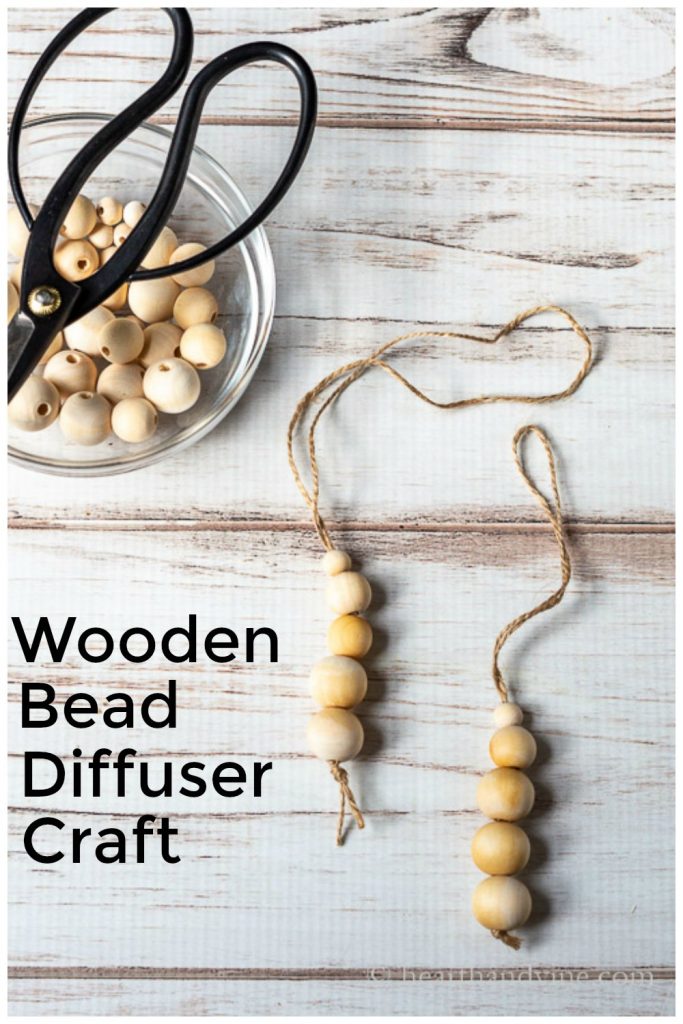 Two wooden bead diffusers on twine next to a bowl of wood beads and a pair of scissors.