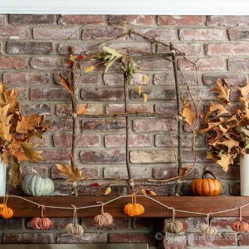 Decorated branch window on mantel with fall leaves and twine pumpkin garland.