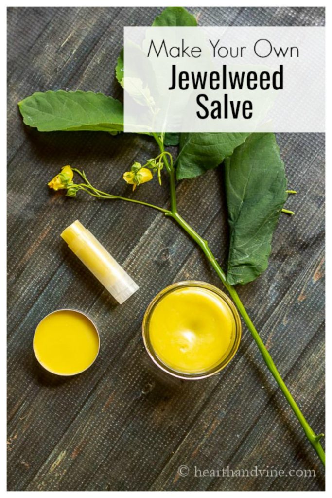 Lip balm tube, small glass container and tin of jewelweed salve next to a branch of impatiens pallida