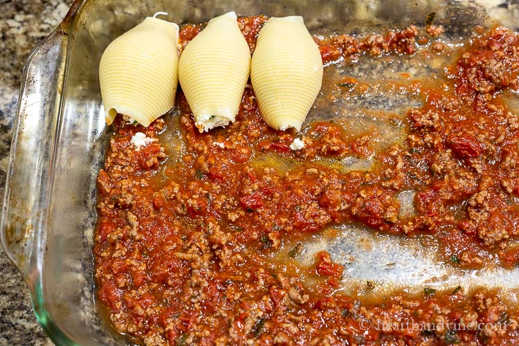 Three stuffed cheese shells set in a pan with meat sauce on the bottom.