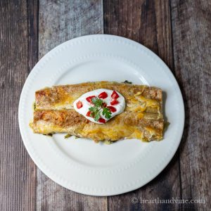 Two spinach enchiladas with sour cream, tomatoes and cilantro on top.