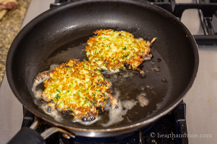 Zucchini pancakes cooking in a frying pan.
