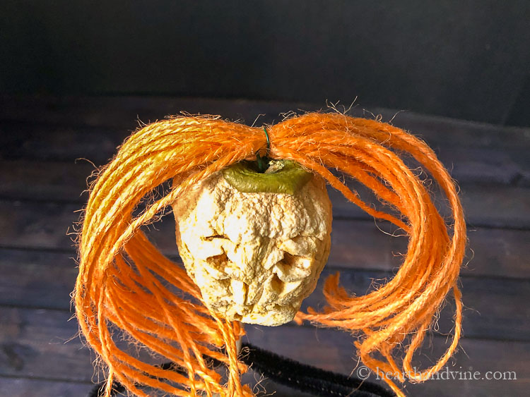 Orange twine pieces gather together in the middle with wire and pushed into the top of the dried apple head for hair.