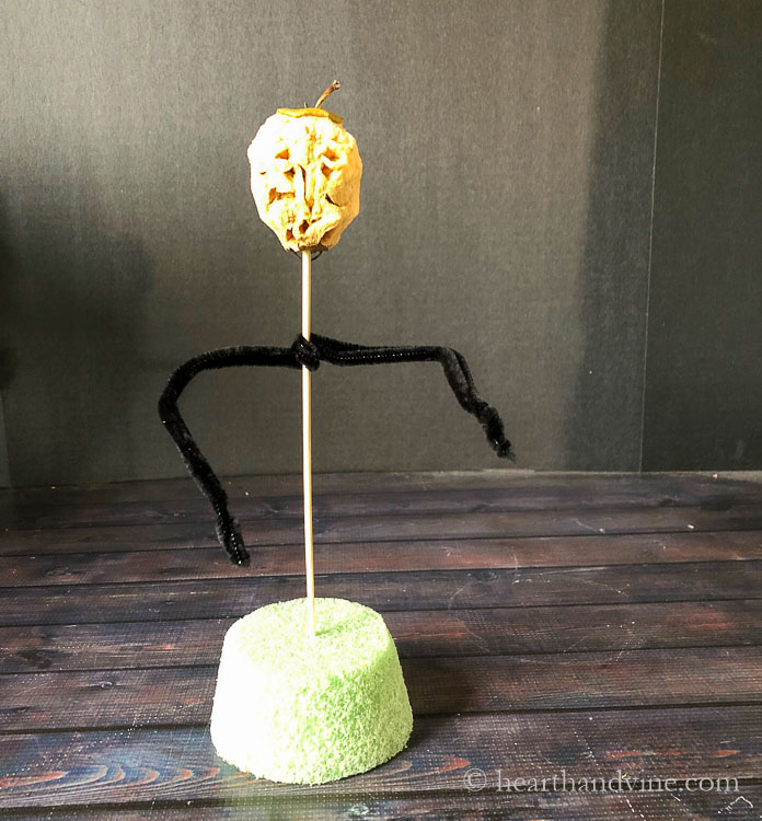 Apple head on top of a wooden skewer. Black pipe cleaners for arms and a round Styrofoam base.