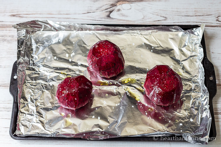 Peeled raw red beets on a cookie sheet with foil, salt and oil.