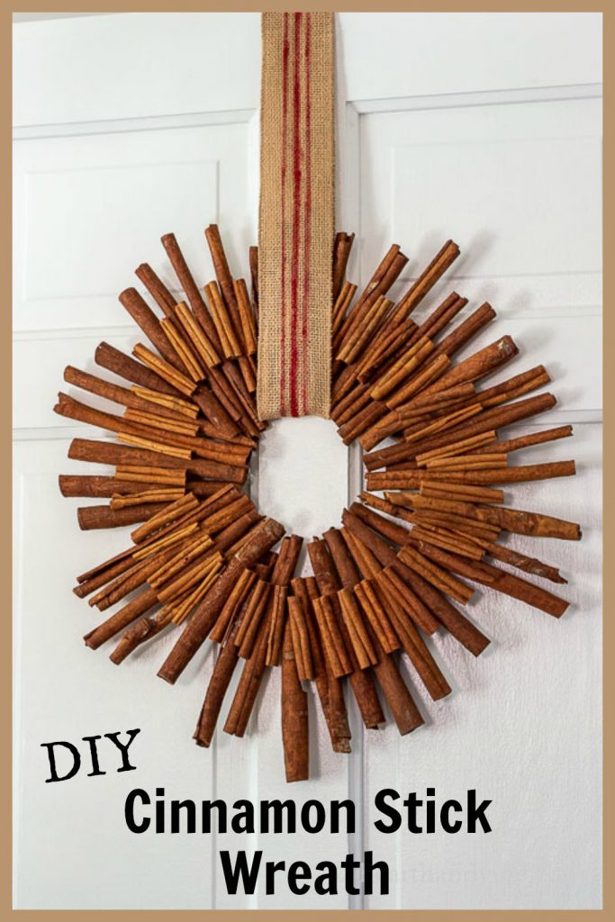 Cinnamon stick wreath hanging from a striped burlap ribbon on a white door.