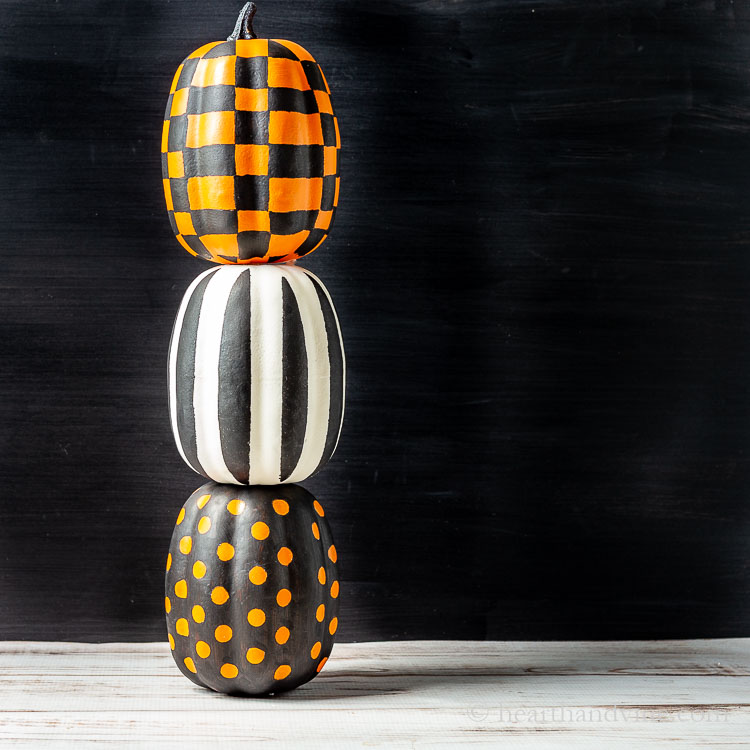 Three different graphically painted pumpkins in shades of orange, black and white, stacked on top of each other.