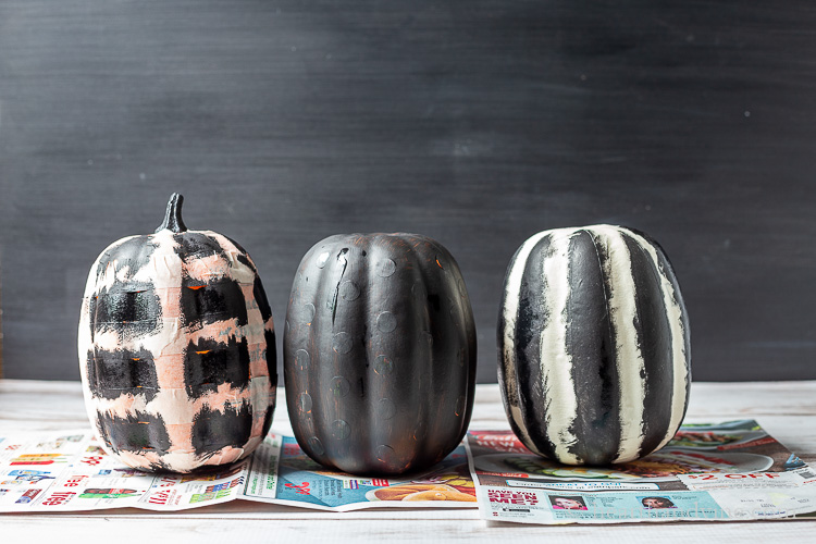 Three craft pumpkins with stickers, or masking tape that have been painted with black paint over top.