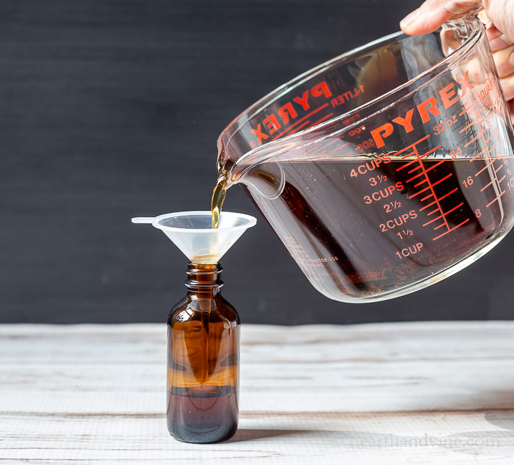 Pouring vanilla extract into an amber glass bottle.