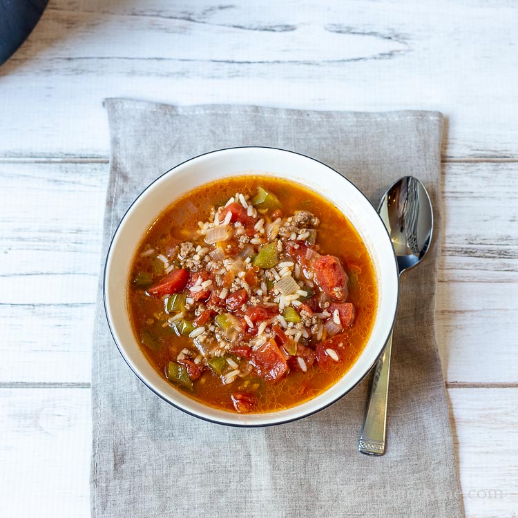 Bowl of stuffed pepper soup on a table with napkin and spoon.