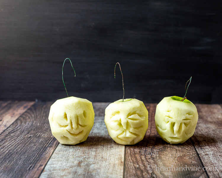 Three peeled apple carved into faces with wire hooks.