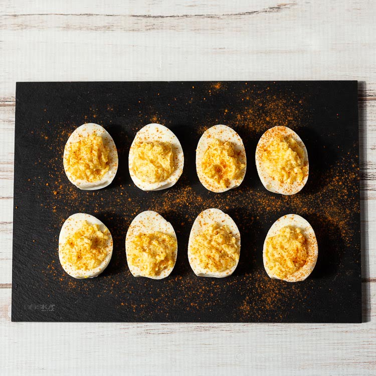 Two rows of deviled eggs with a ground paprika dusting.