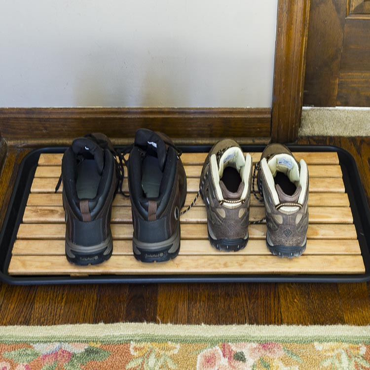 Wooden slat boot tray in foyer with two sets of boots.