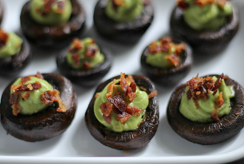 Tray of stuffed mushrooms with avocado cream and bacon.