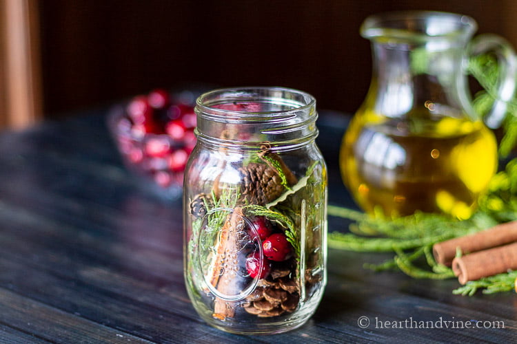 Mason jar stuffed with cranberries, cinnamon sticks, pine cones and cedar.