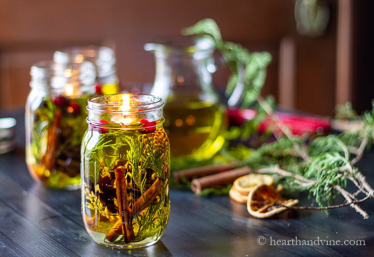 Oil candle in a mason jar with natural elements like cinnamon stick cedar tips and pine cones suspended in olive oil with a floating wick.