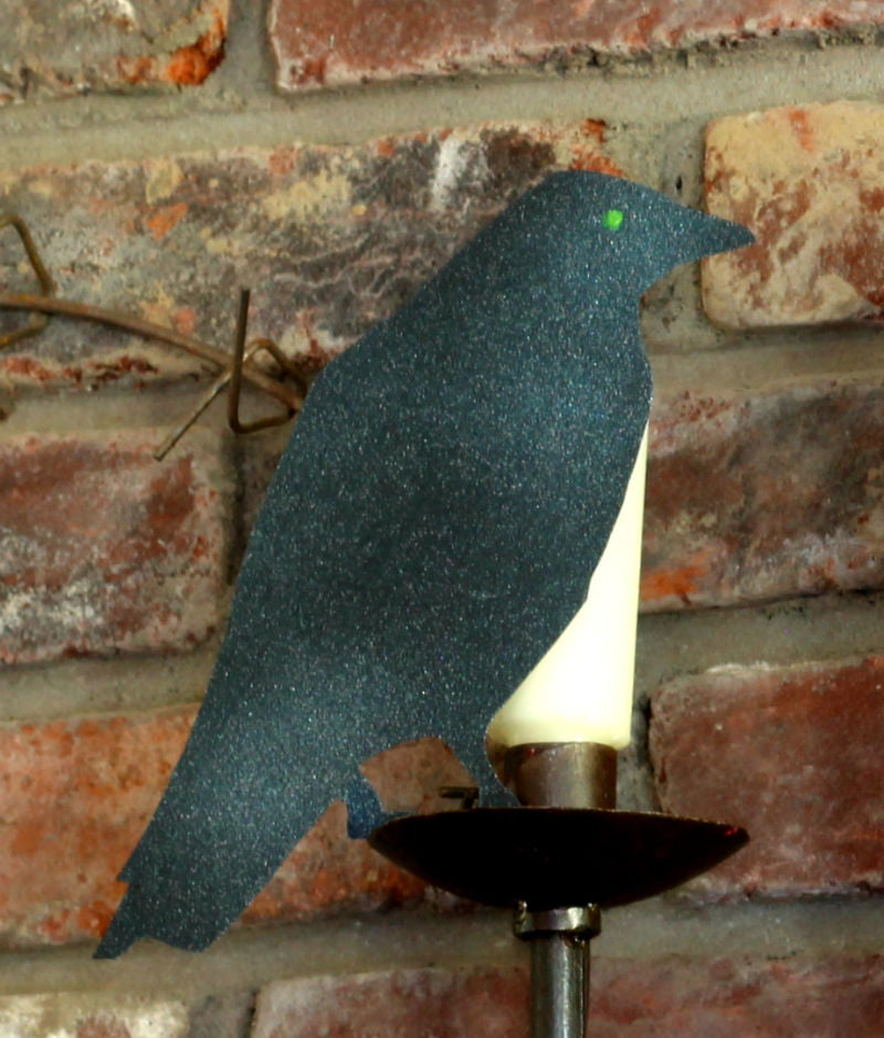 Halloween black crow with glowing green eye on mantel.