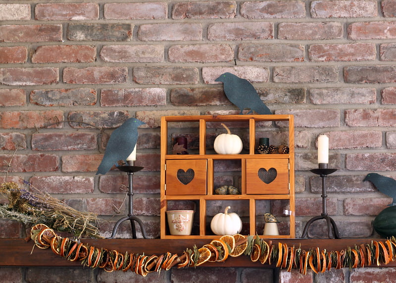 Family mantel decorated for Halloween with dried fruit, pumpkins and paper crows.