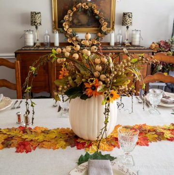 Decorated Thanksgiving table with pumpkin vase filled with flowers, a leaf runner and real oak leaves.
