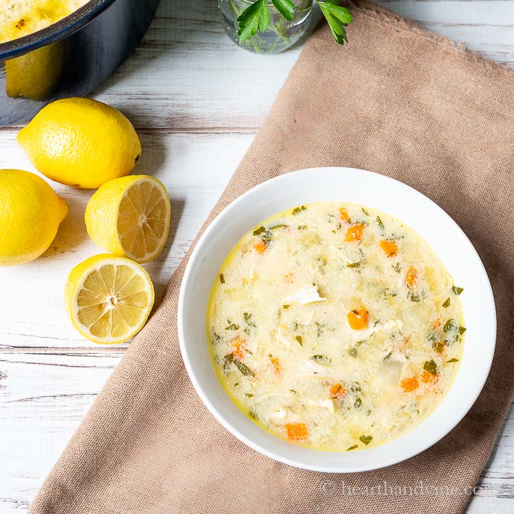 Bowl of lemon chicken Greek orzo soup next to some lemons and the corner of the pot of soup.