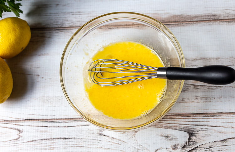 Glass mixing bowl with eggs, lemon juice and wire whisk.