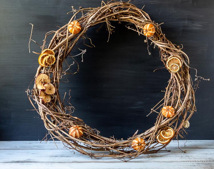 Grapevine wreath with a few dried mandarin oranges and some stacked orange slices and apple slices.