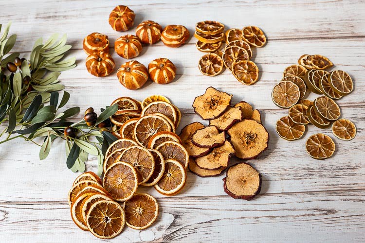 Faux greenerybranches, dried mandarins, orange slices, and apple, lemon and lime slices on a table.