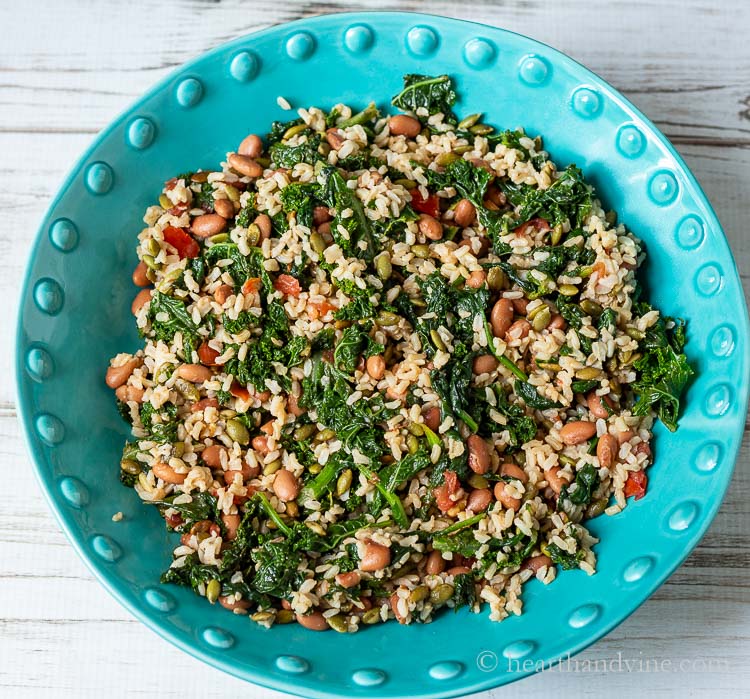 Blue bowl with mixed greens and grains, beans, and pumpkin seed kernels.