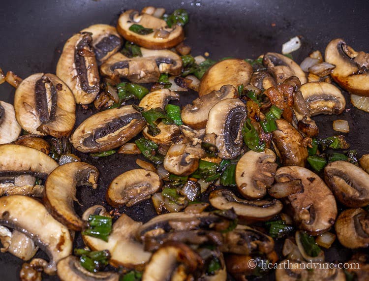 Mushrooms, onions and chopped shishito peppers sautéing in a large pan.